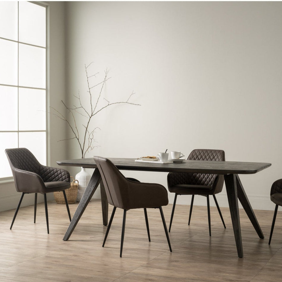 Dining table with four chairs in a modern room with large windows.
