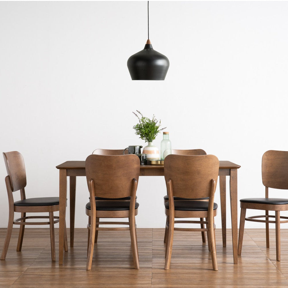 A dining set consisting of a rectangular wooden table and four matching chairs with black seat cushions, arranged in a minimalist room with a white wall and light wood floor under a black pendant light.