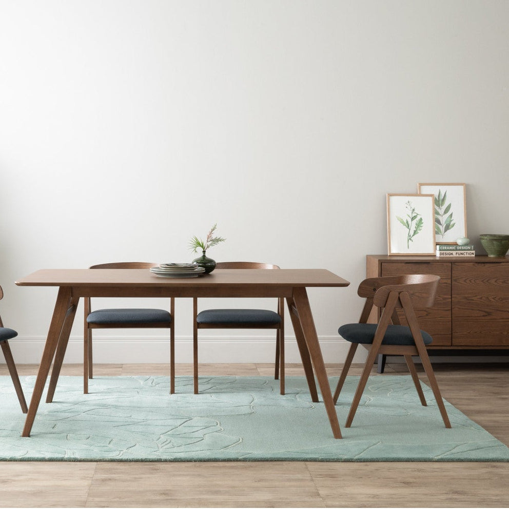 Dining room with wooden table and chairs on a light green rug, plants, and a sideboard.