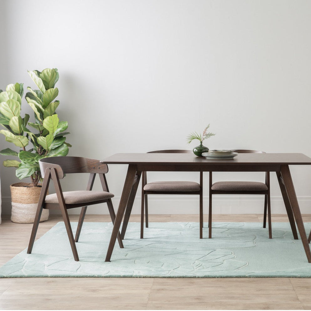 Dining room with wooden table and chairs on a light green rug, plants, and a sideboard.