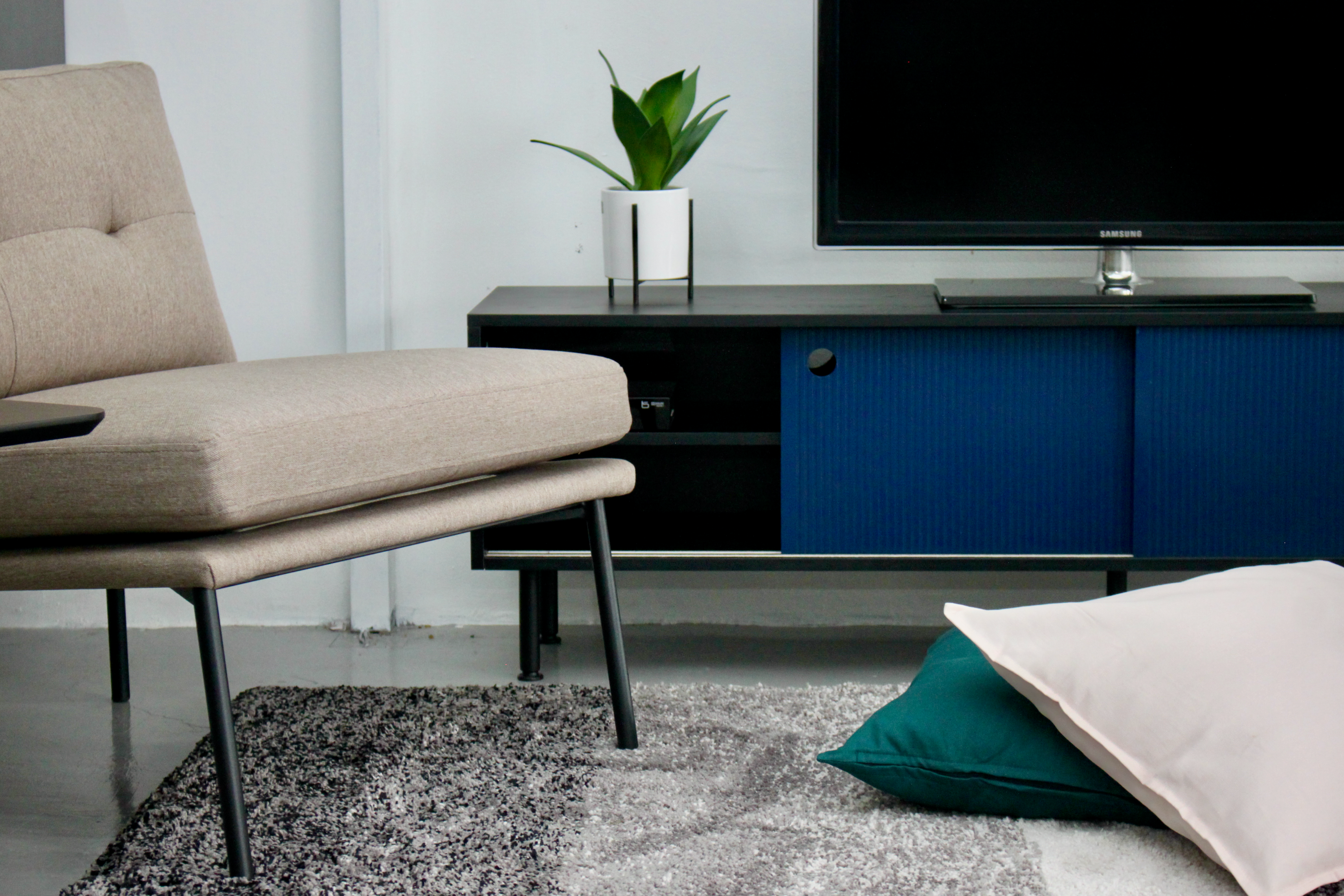 A modern TV cabinet with a black body and dark blue doors, featuring a flat-screen TV on top and a beige sofa in front.