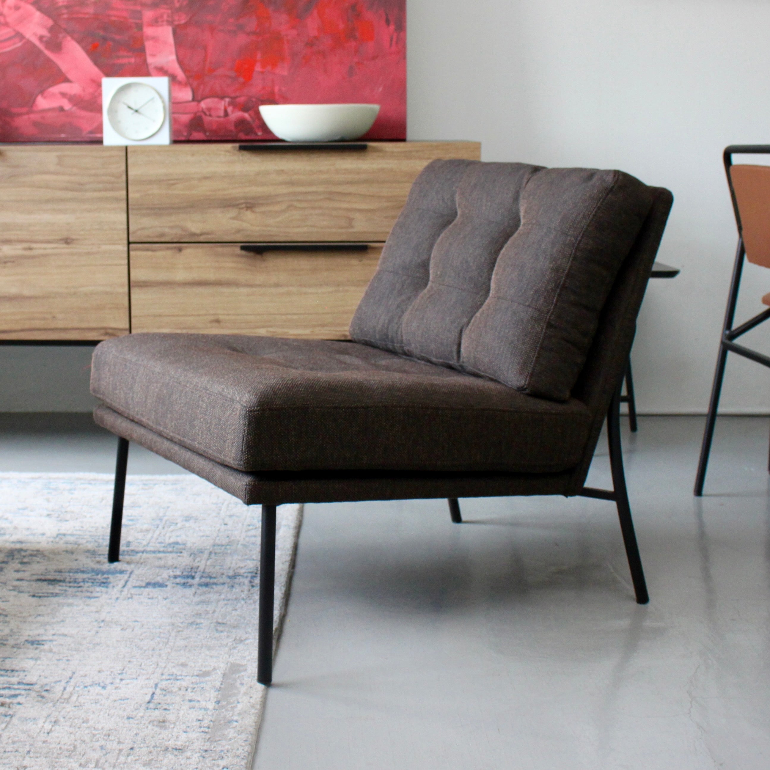 A brown fabric arm chair with a tufted backrest and metal legs, placed in a modern living room setting.
