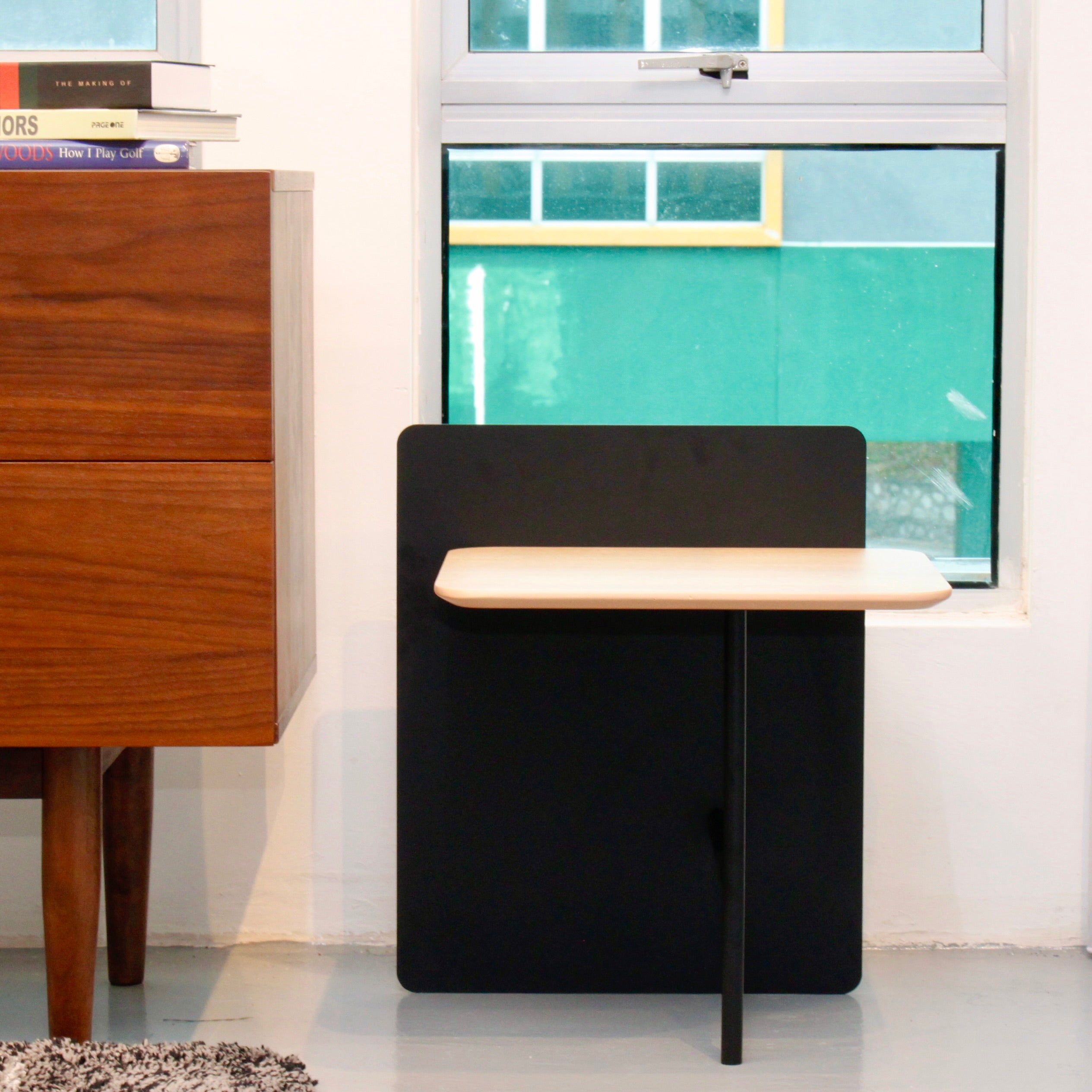 A side table with a walnut tabletop and black metal frame, positioned next to a window and an wooden cabinet.