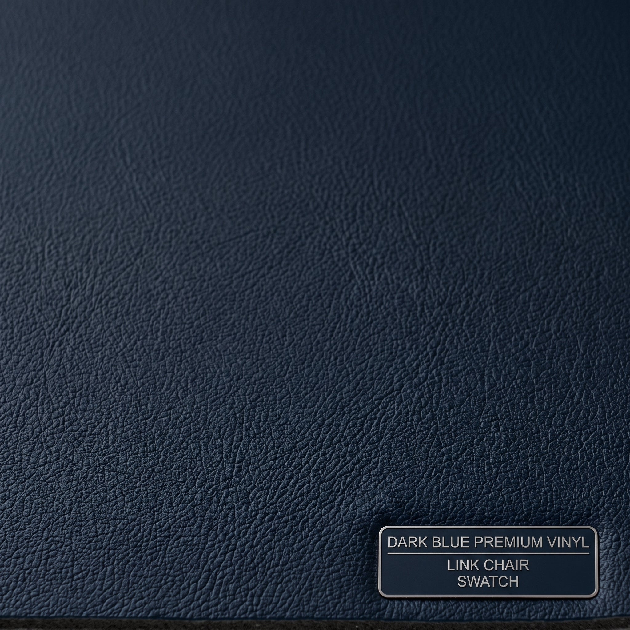 A close-up texture swatch of dark blue premium vinyl with a fine grain finish, featuring a small label in the bottom right corner that reads 'DARK BLUE PREMIUM VINYL LINK CHAIR SWATCH'.