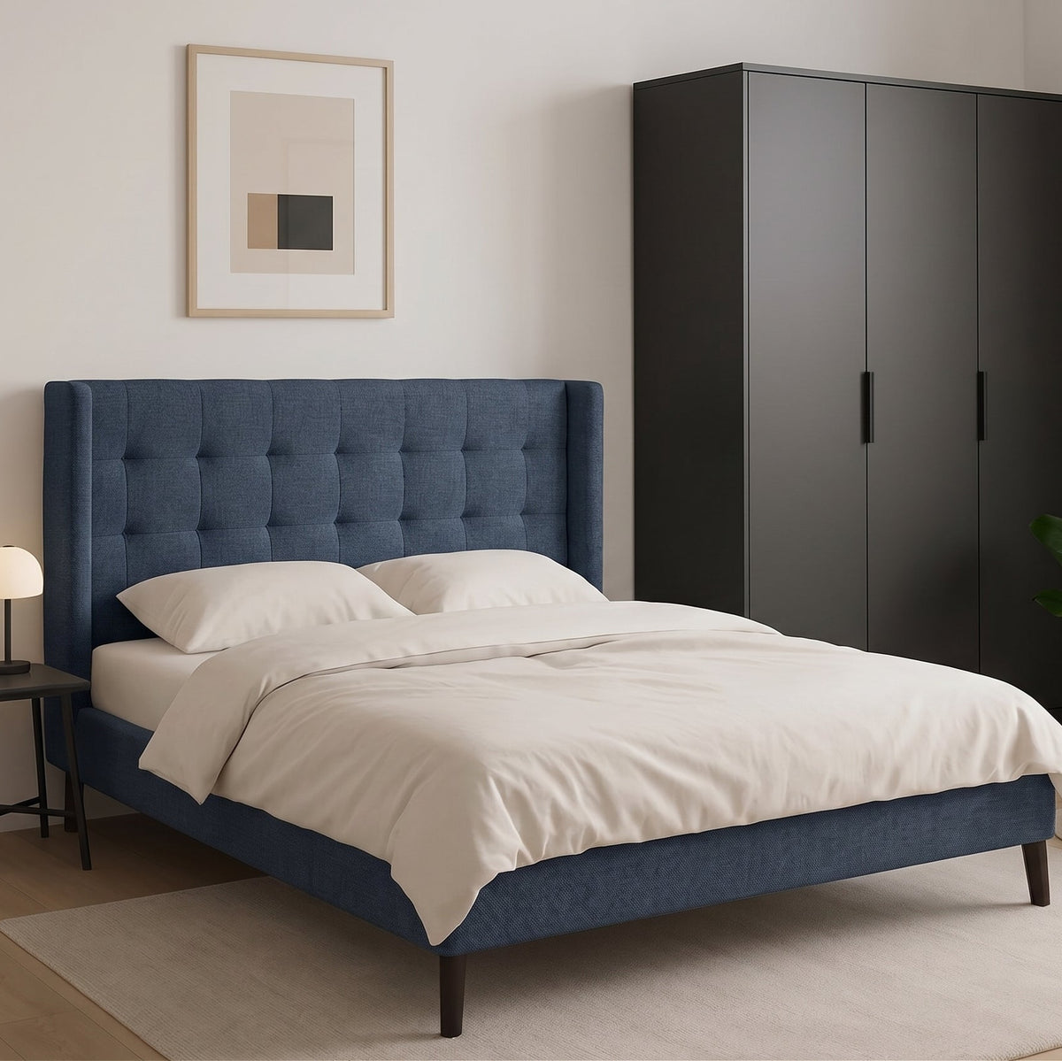 A modern bedroom scene featuring a blue tufted bed frame with white bedding, a tall dark gray wardrobe, a brown leather armchair, and a small side table with a lamp.