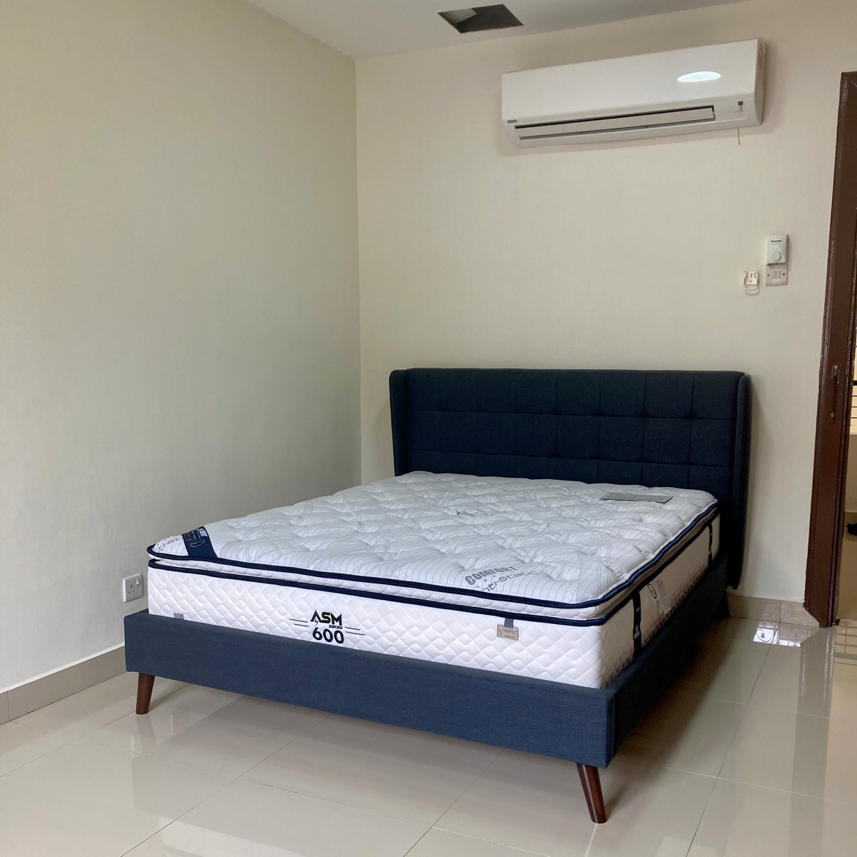 Bed with mattress in a room with a white wall and tiled floor.