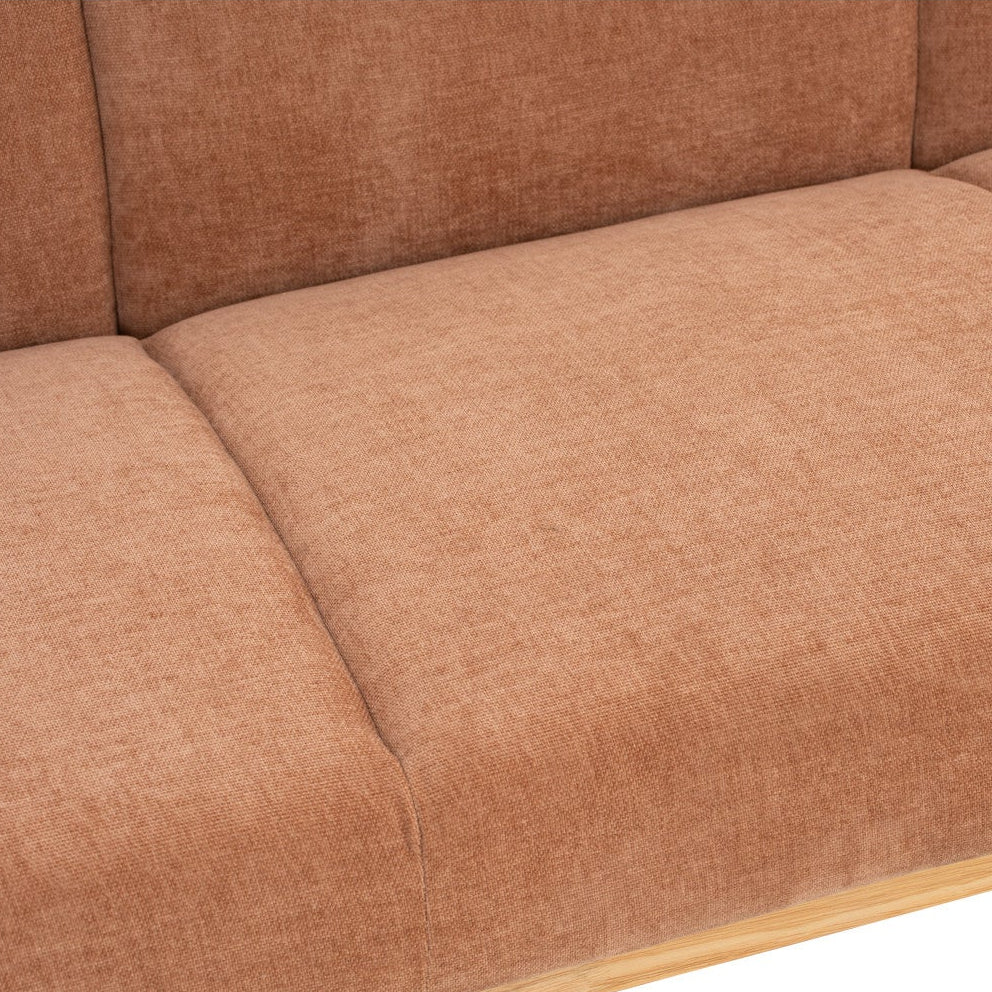 Close-up of a sofa seat cushion in a warm rust-brown textured fabric, showing the tufted panel seams and a light wood edge against a white background.