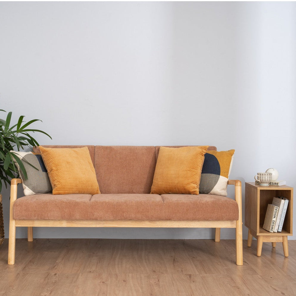 A modern wooden loveseat sofa with a textured orange-brown fabric, styled with mustard yellow and gray accent pillows, set in a minimalist room with a potted plant on the left and a small wooden side table on the right.