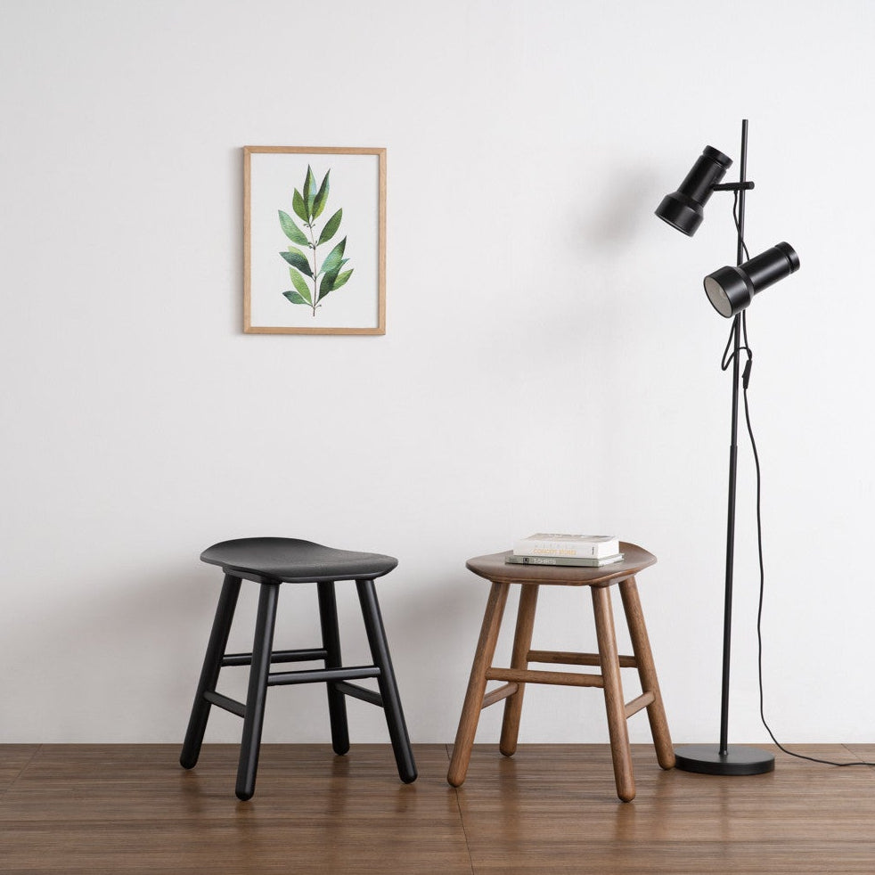 Two stools and a floor lamp against a white wall with a framed picture.