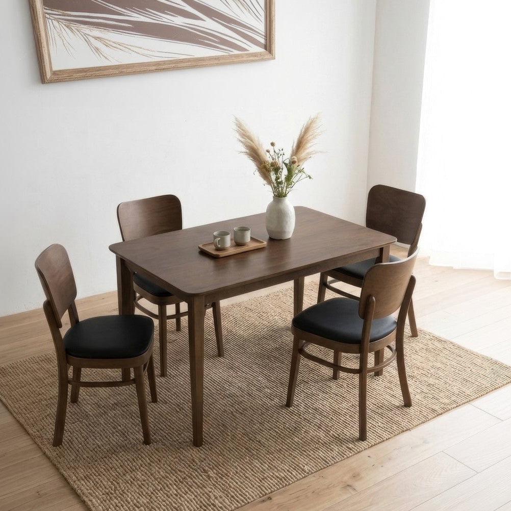 A 5-piece dining set consisting of a rectangular wooden table and four matching chairs with black cushioned seats, styled on a jute rug in a bright, modern room with a potted plant.