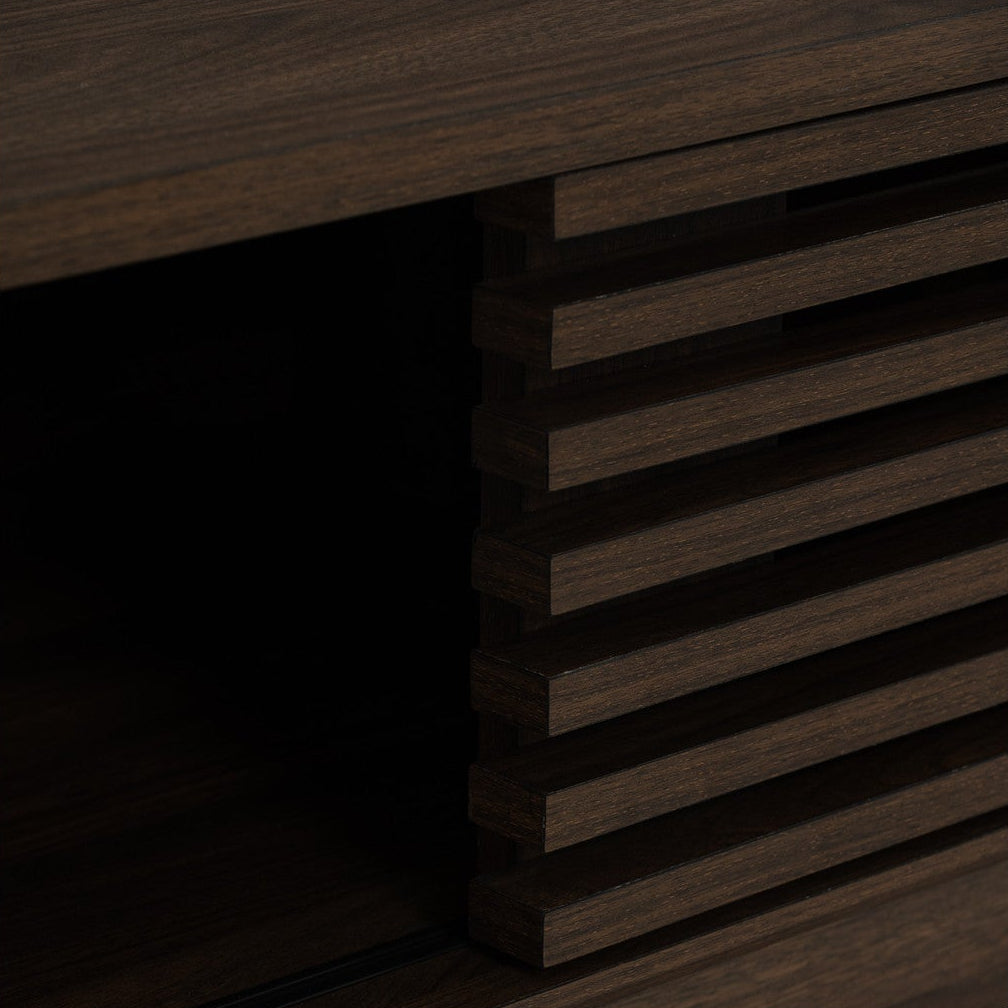 Close-up of a dark brown wood cabinet or shelf unit showing a slatted front panel and an open storage compartment on a white background.