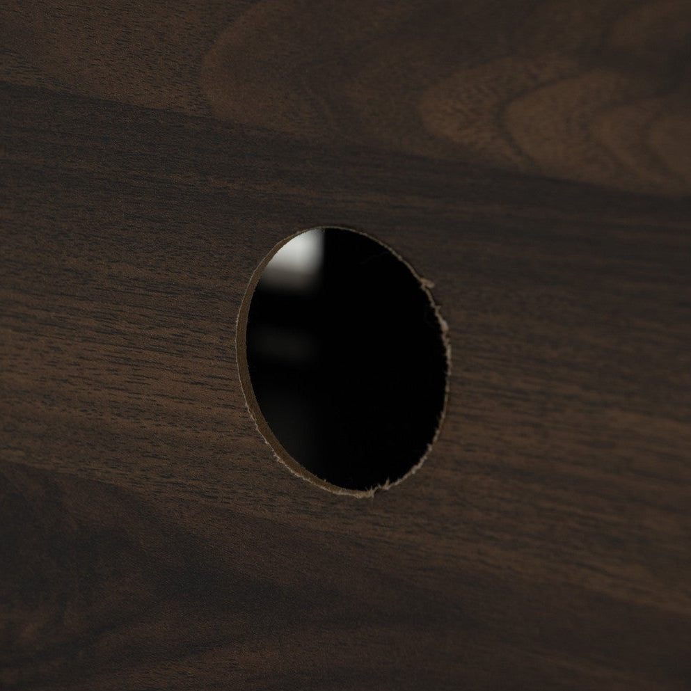 Close-up of a dark brown wood surface with a circular cutout hole showing a black interior.