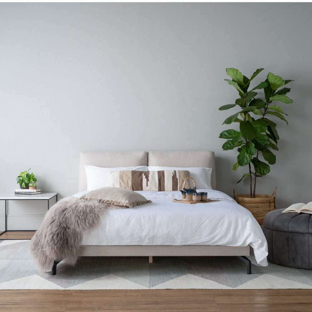 Modern bedroom with a bed, side table, and plant against a gray wall.