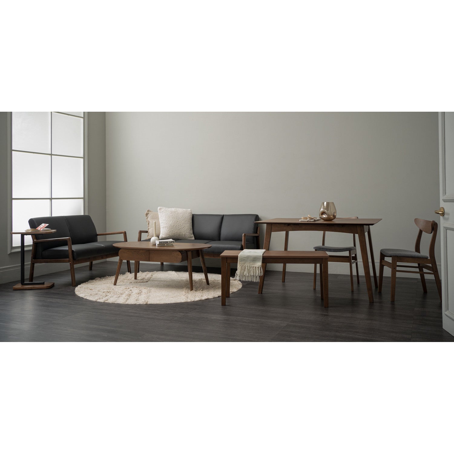 A mid-century modern furniture set in a minimalist living room, featuring a dark gray sofa, matching armchair, wooden dining table, wooden coffee table, and wooden chairs on a dark wood floor with a light rug.
