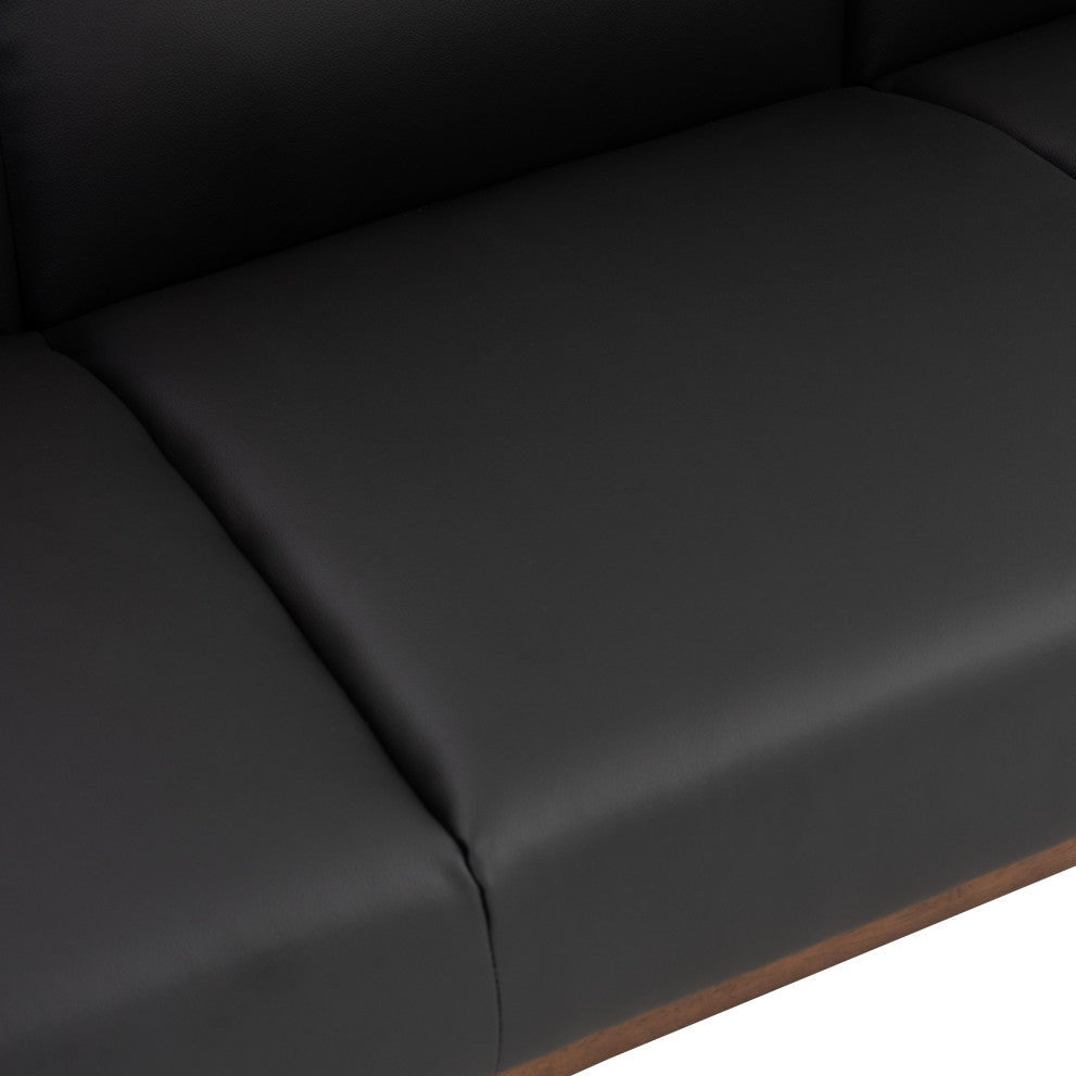 Close-up of a black upholstered sofa seat cushion with visible seam lines and a small portion of a brown wooden base edge against a white background.