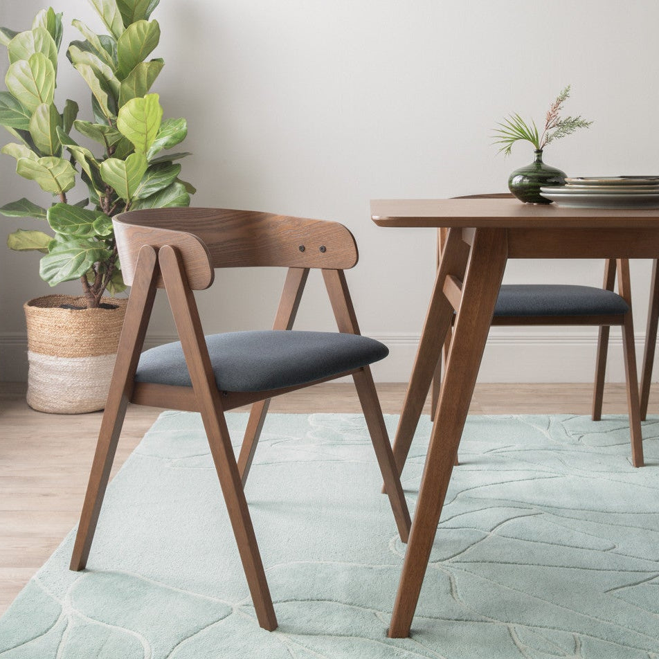 Dining room with wooden table and chairs on a light green rug, plants, and neutral decor.