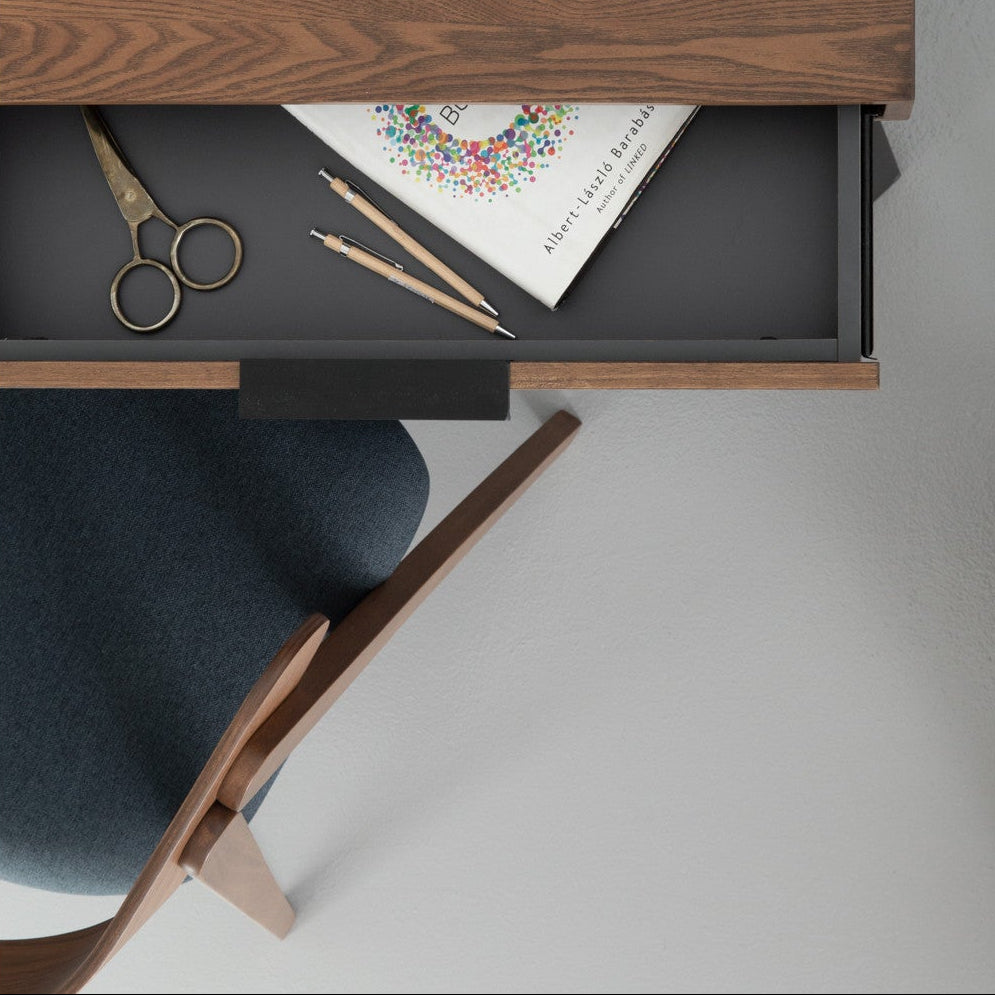 Wooden desk with open drawer containing stationery items on a white background