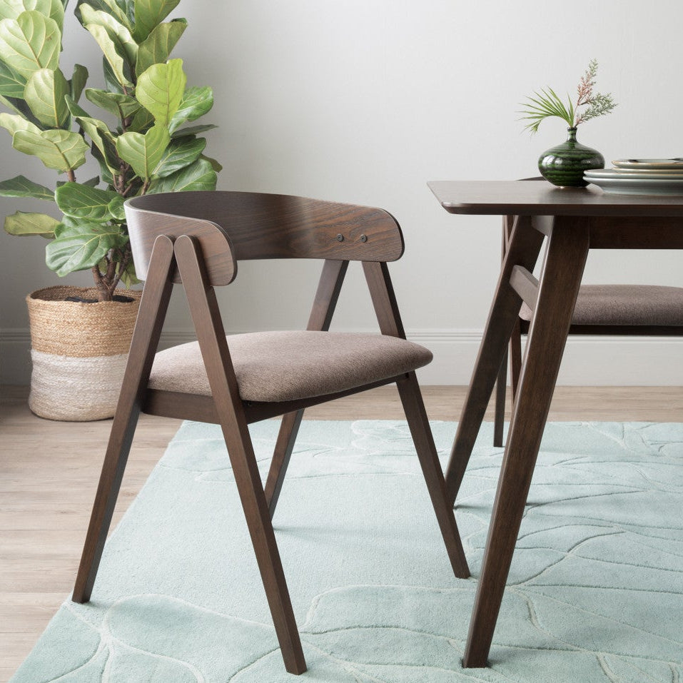Dining room with wooden table and chairs, potted plant, and light green rug.