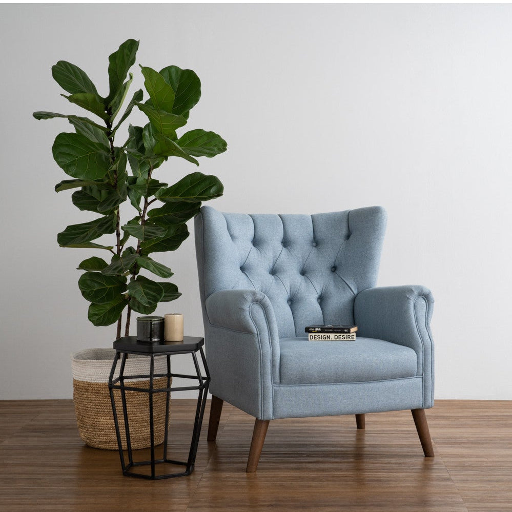 Blue armchair with a plant and small table in a room with wooden flooring and white walls.