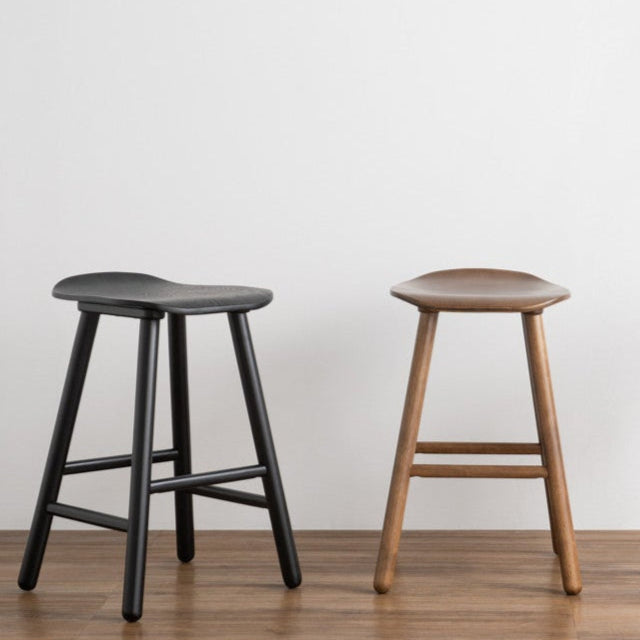 Three stools in different colors on a wooden floor with a white wall background