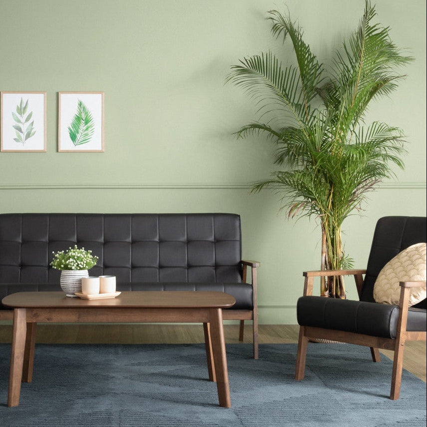 Modern living room with black sofa, armchairs, and a coffee table against a green wall.