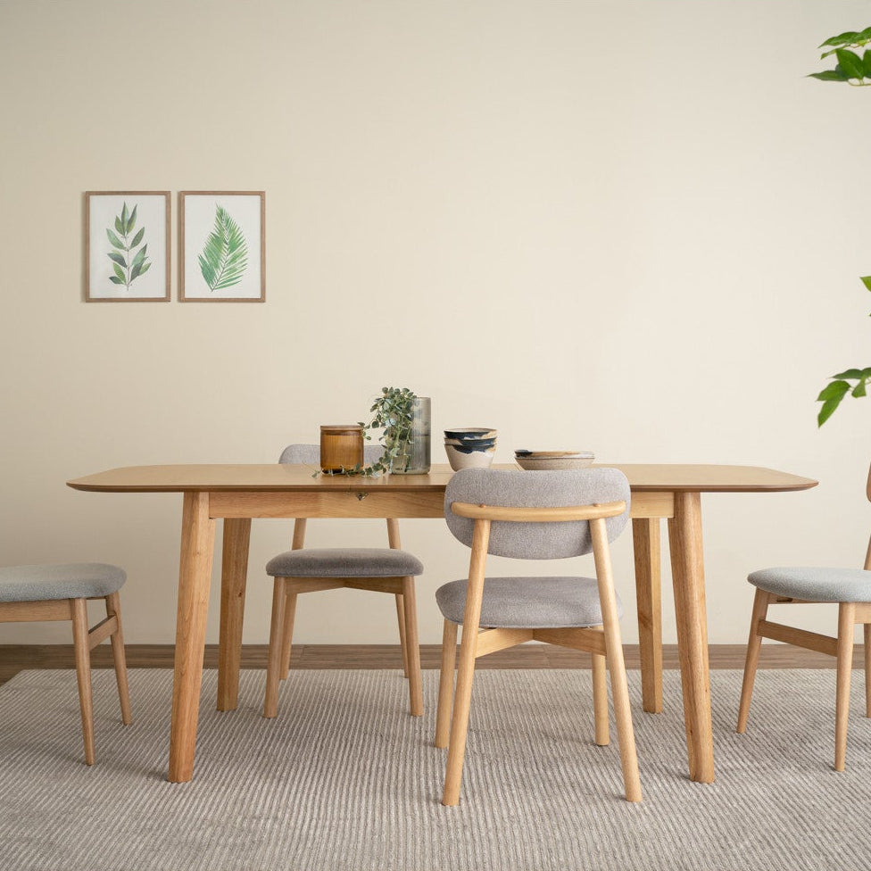 Dining room with wooden table and chairs on a light gray rug, plants, and wall art.