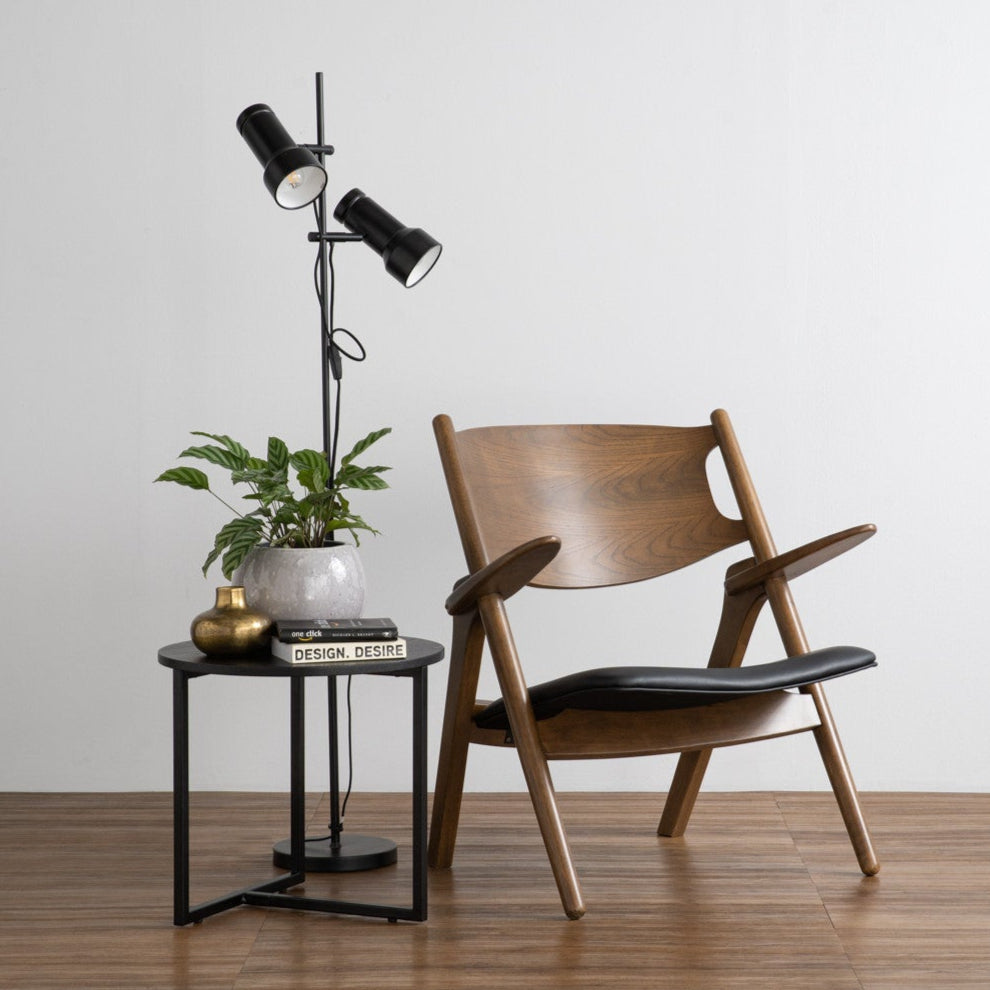 Wooden chair with black seat and backrest in a room with a floor lamp and small table.