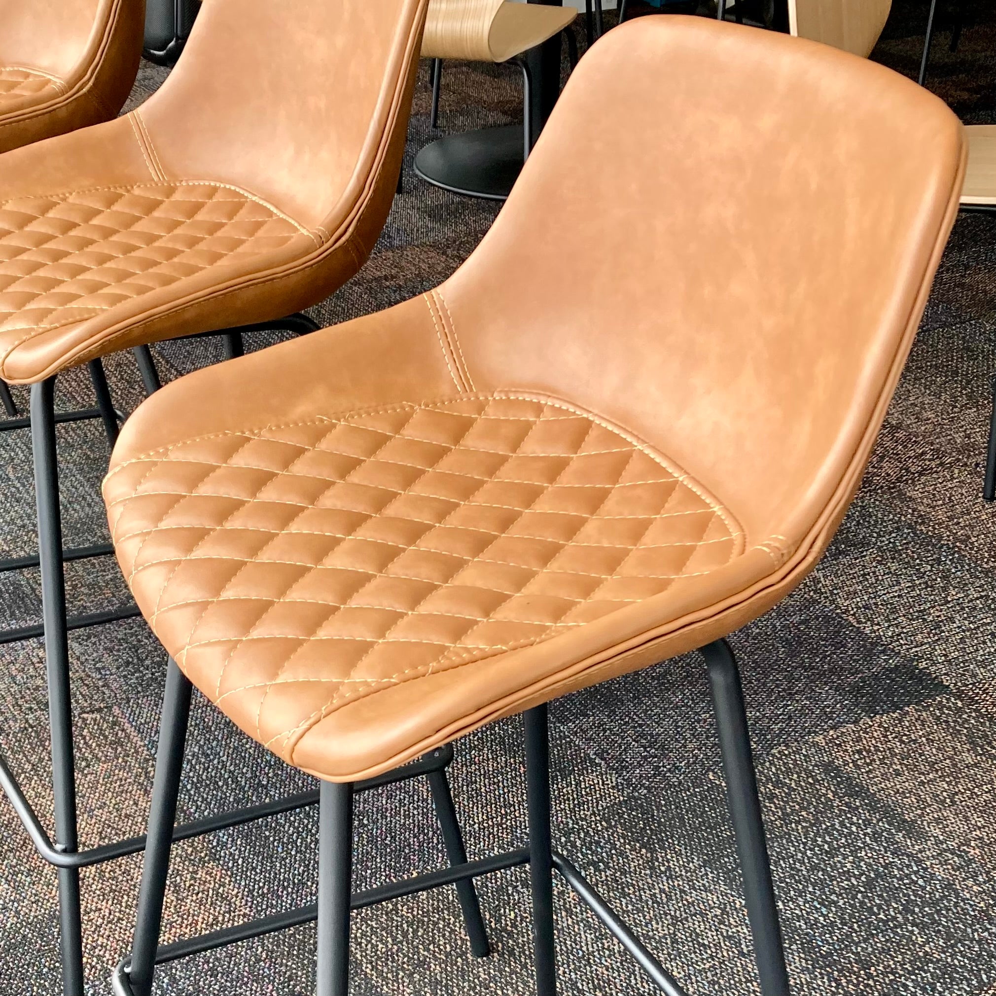 Brown quilted leather stools with black metal legs on a textured floor.