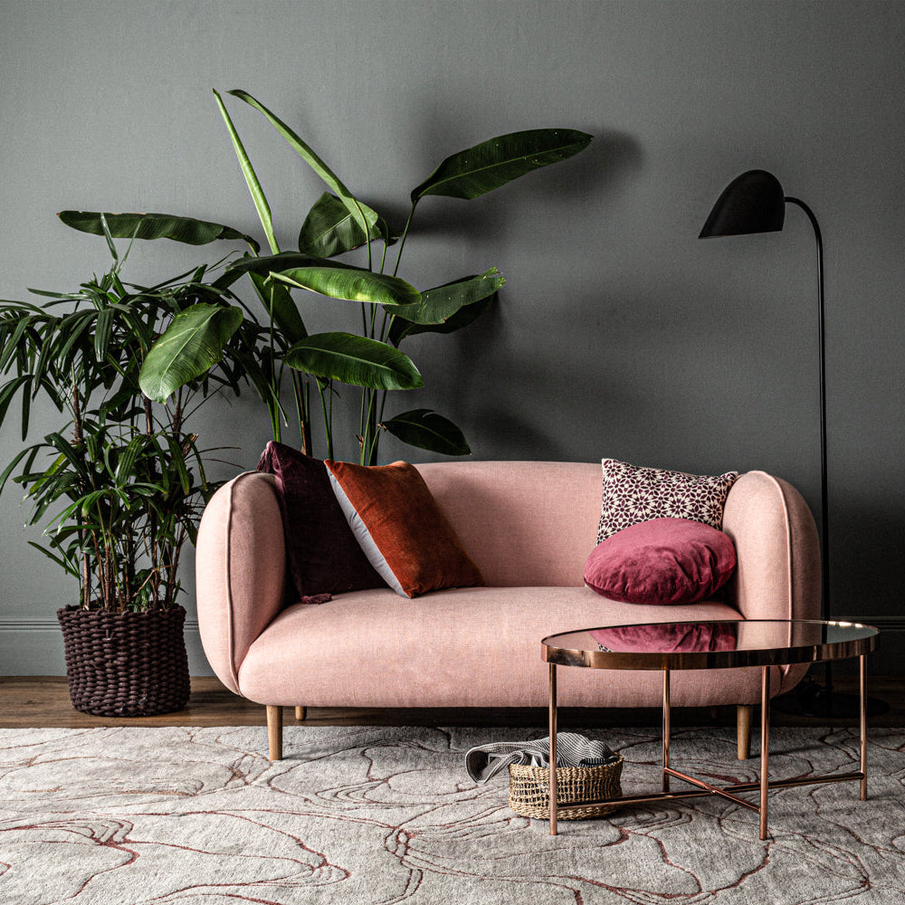 Pink sofa with decorative pillows in a room with a dark wall, plant, and coffee table.