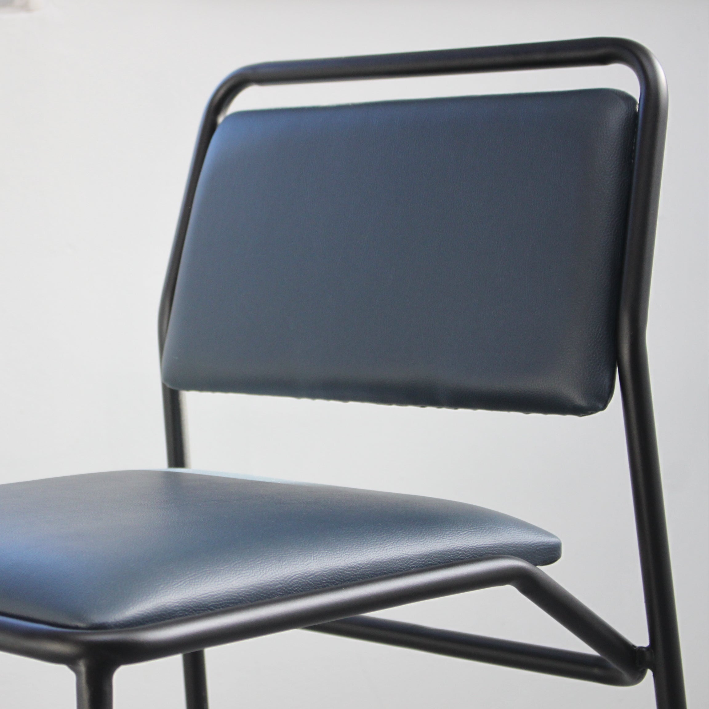 A modern dining chair with a black metal frame and dark blue-gray padded seat and backrest, shown against a plain light gray wall.