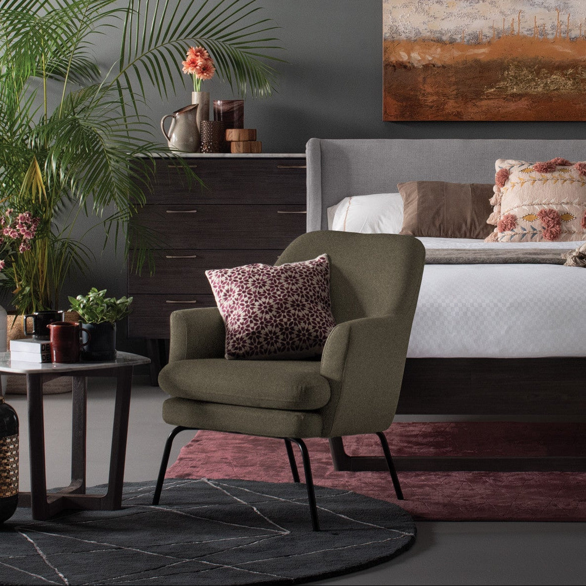 Modern bedroom with a green armchair, floral pillows, and a abstract painting on the wall.