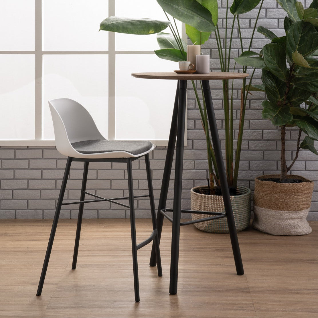 Modern indoor setting with a high stool, small table, and potted plants against a brick wall.