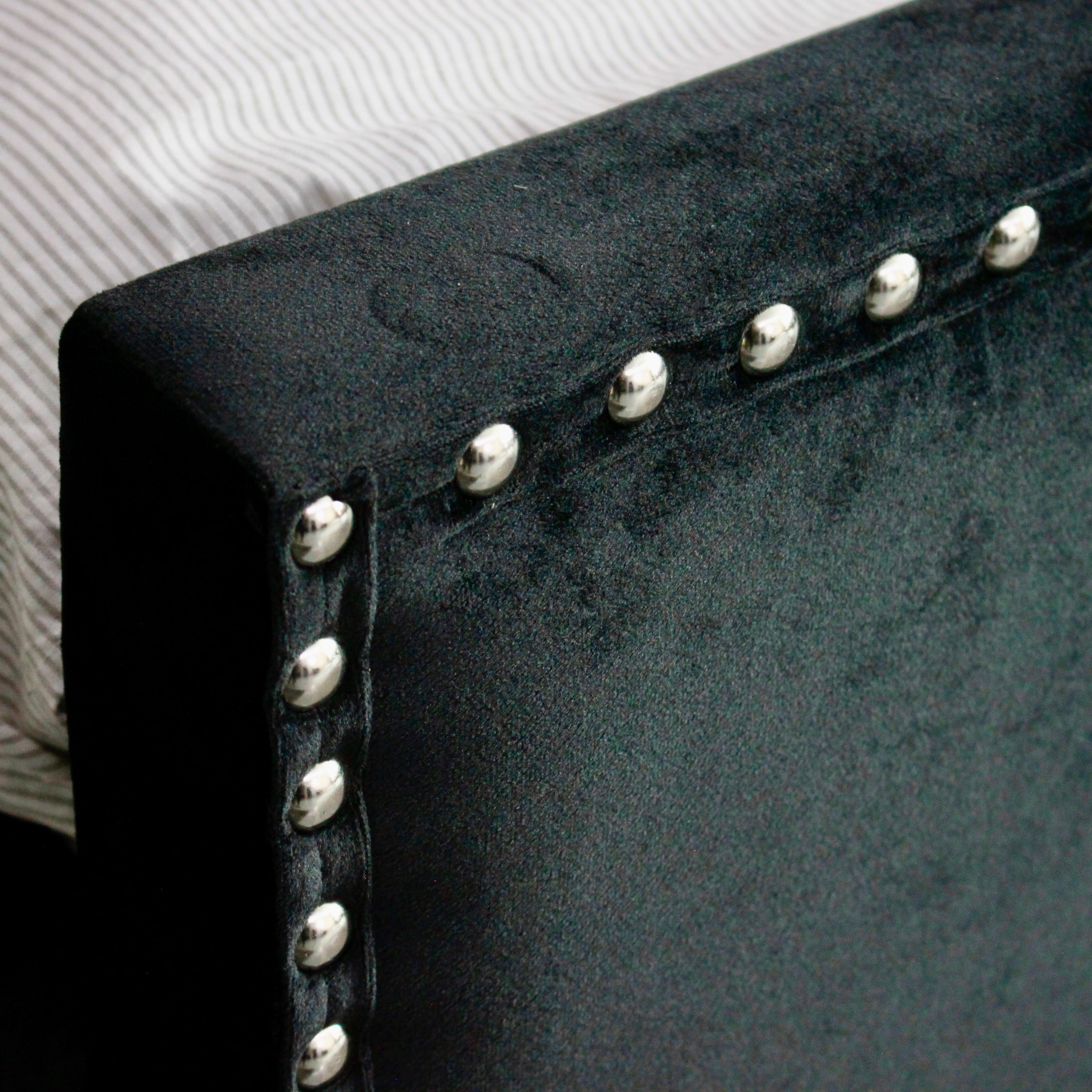 Close-up of a black upholstered footboard with silver nailhead trim.