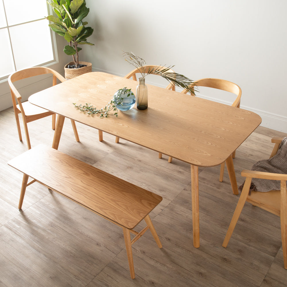 A light natural wood dining set in a bright, modern room, featuring a rectangular table, a matching bench, and four chairs.