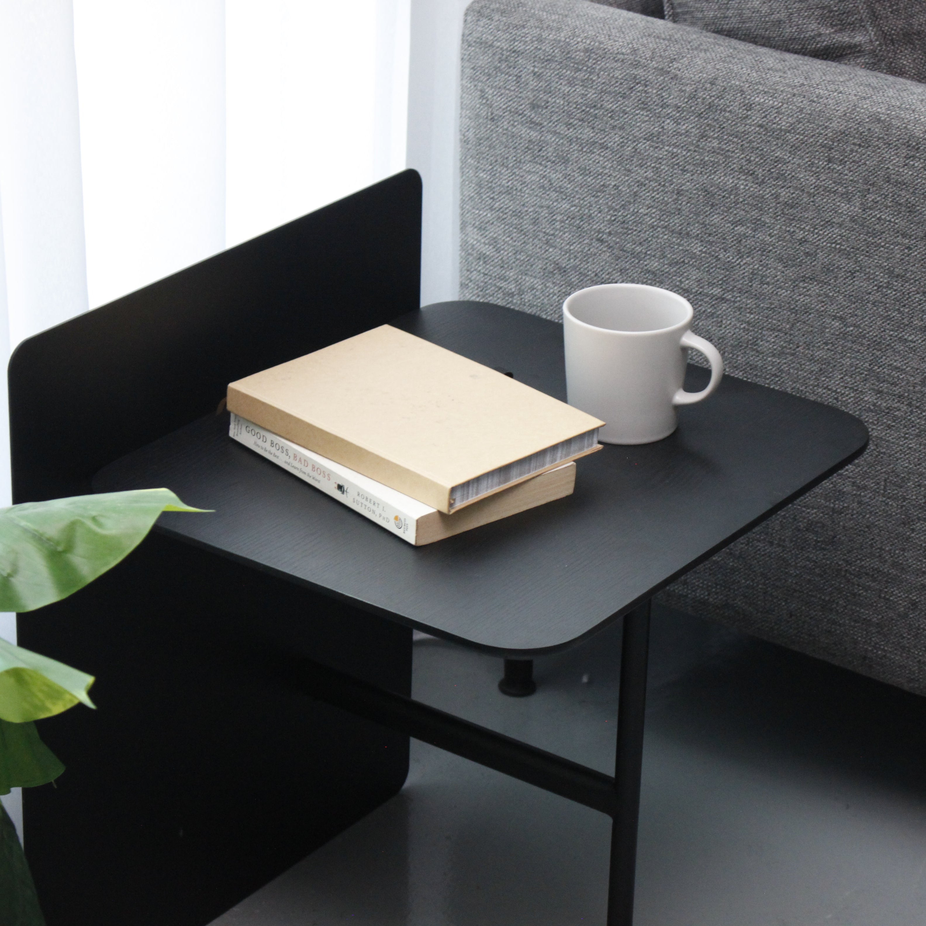 Black side table with a book and white mug next to a gray sofa
