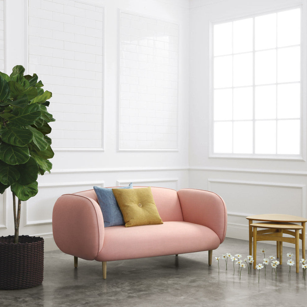 Modern pink sofa with colorful cushions in a bright room with a plant and small table.