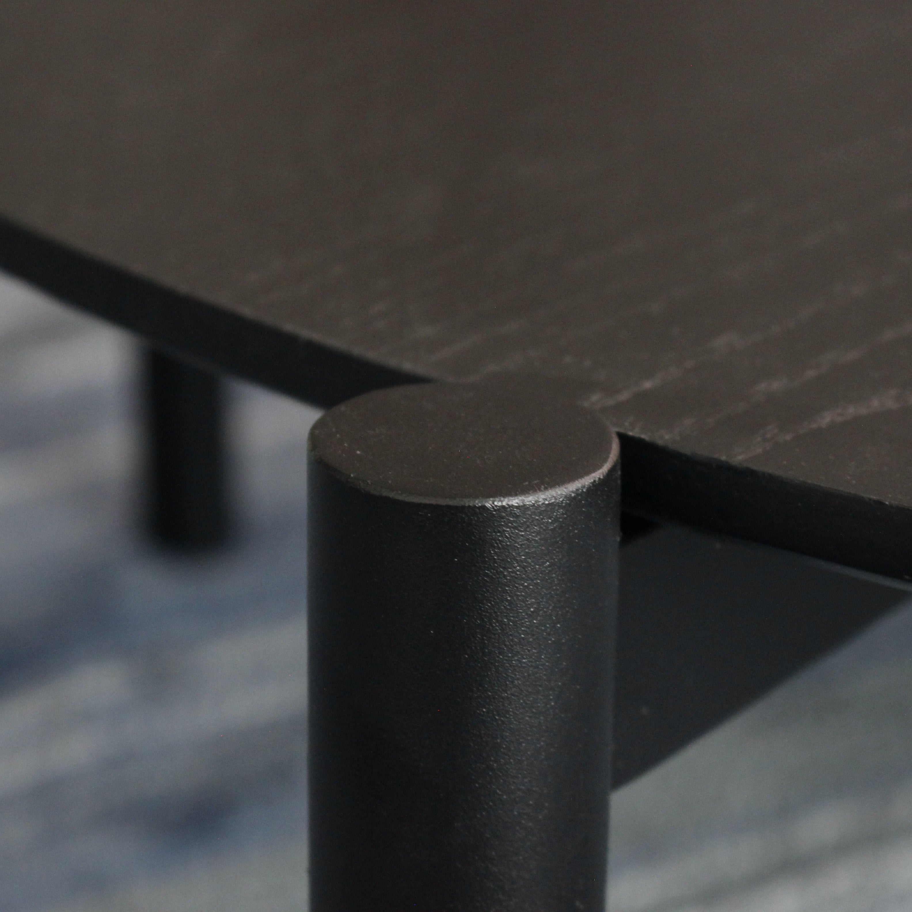 Close-up of a black metal table leg and top with a blurred background