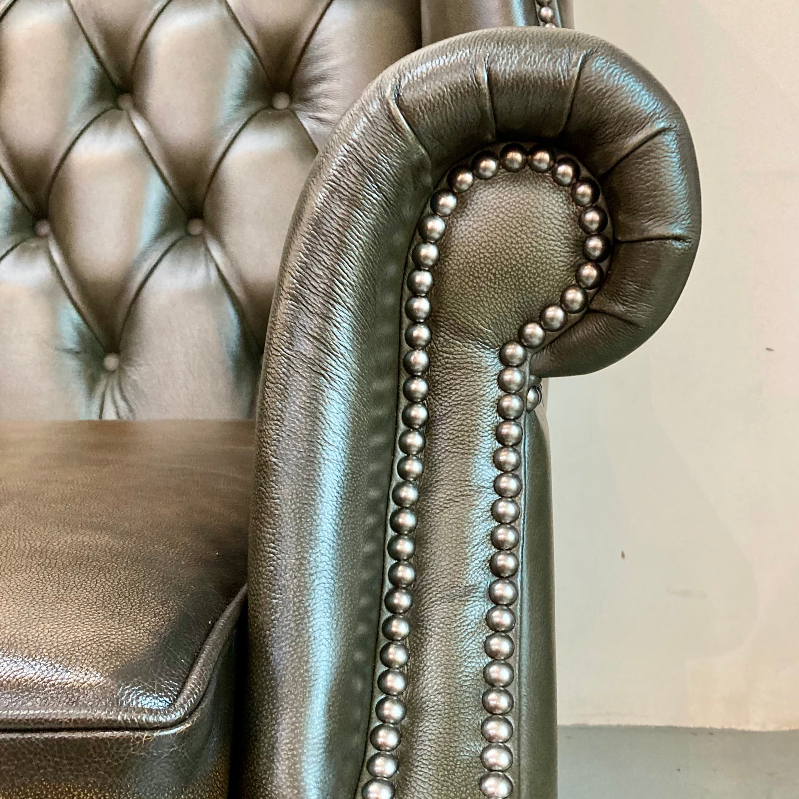 Silver tufted armchair with decorative bead trim against a neutral wall.