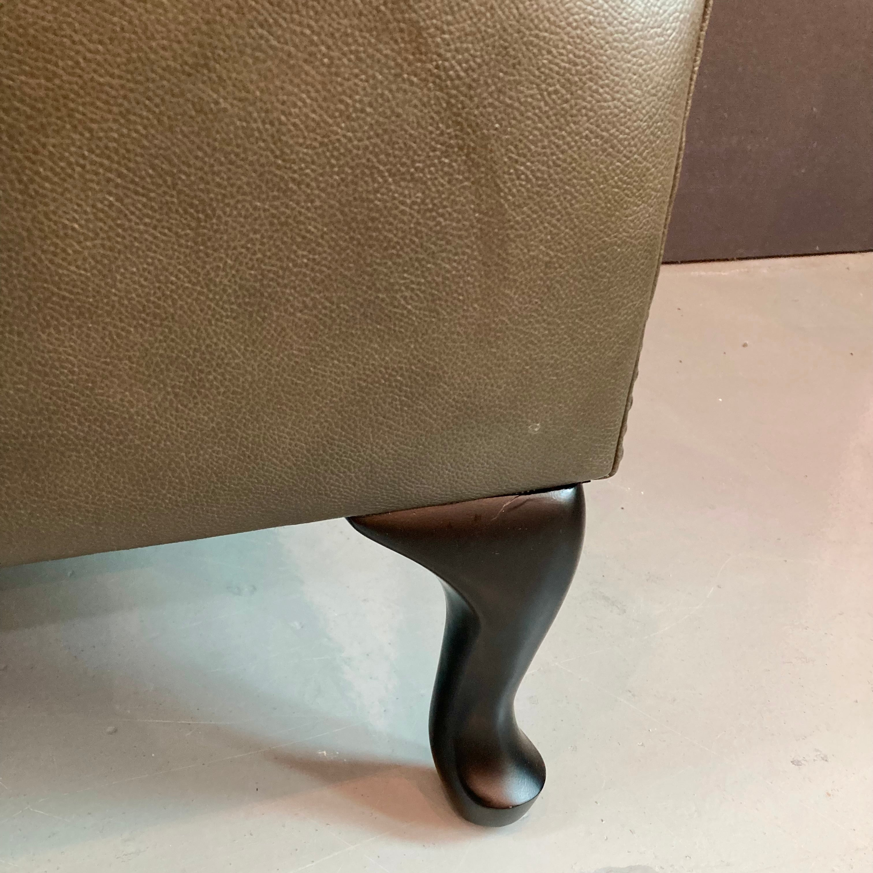 Close-up of a brown leather armchair with a dark wooden leg on a light-colored floor.
